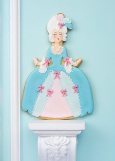 a cookie shaped like a woman in a blue dress on a white shelf next to a light blue wall