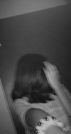 a woman standing in front of a mirror holding her hands to her face and looking at herself