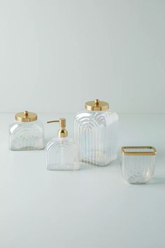 three clear glass containers with gold accents on the top and bottom, one is empty