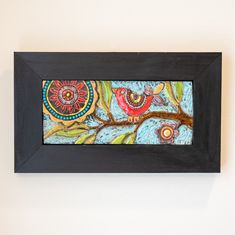 a painting hanging on the wall next to a black frame with an owl and flowers painted on it