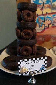 a stack of chocolate donuts sitting on top of a plate next to a sign