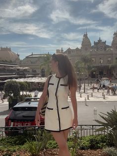 a woman in a short white dress is standing on the side walk near a street