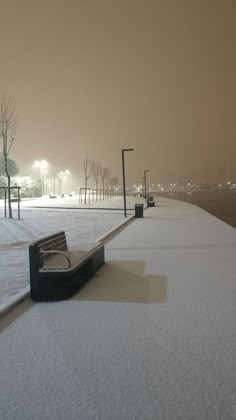 a bench sitting on the side of a snow covered road next to a street light