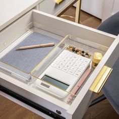 a drawer with a calculator, pen and pencils in it on top of a desk