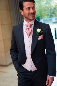 a man in a tuxedo smiles at the camera while wearing a pink bow tie