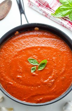 a bowl of tomato soup with basil leaves on top and spoons next to it