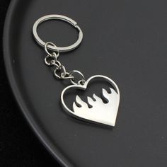 a metal heart shaped keychain with flames on the front and back sides, sitting on a black surface