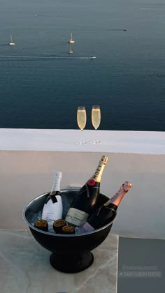 two champagne flutes are sitting in a bowl on a balcony overlooking the ocean and sailboats