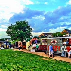 people standing in front of food trucks parked on the side of a road near grass