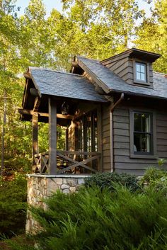 a house in the woods surrounded by trees and bushes with a covered porch on one side