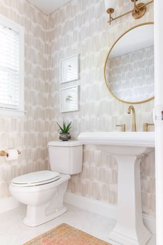 a white toilet sitting next to a sink in a bathroom under a mirror with a gold faucet