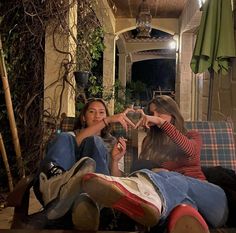 two young women sitting on a couch making the shape of a heart with their hands