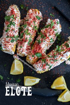 mexican elote on a black plate with lemon wedges and cilantro sprinkles