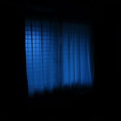 a dark room with blue curtains and a bed