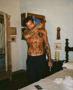 a man with tattoos on his body standing next to a bed