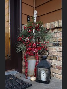 a potted plant sitting next to a lantern on the front porch with pine cones and berries