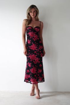 a woman standing in front of a white wall wearing a black and pink floral dress