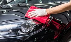 a person wiping the hood of a black car with a red microfibrel