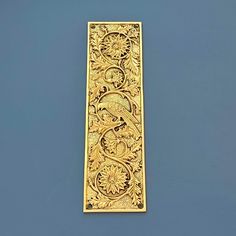 an ornate gold bookmark on a blue surface with flowers and leaves in the center