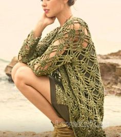 a woman sitting on top of a beach next to the ocean wearing a green crocheted sweater