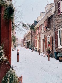 a snowy street lined with brick buildings and christmas wreaths on the windows sill