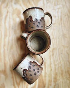 two coffee mugs sitting on top of a wooden table with holes in the middle