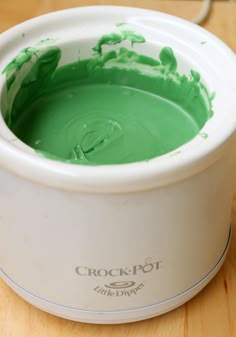 a white bucket filled with green paint on top of a wooden table