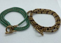 two green and gold beaded bracelets sitting next to each other