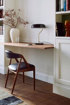 a desk with a chair, lamp and vase on it