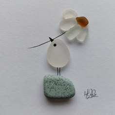 a white bird sitting on top of a green rock next to a leaf and flower