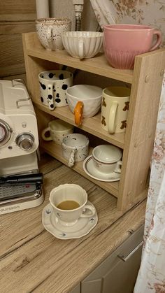 a coffee maker sitting on top of a wooden counter next to cups and saucers