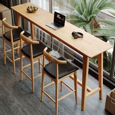 a wooden table with four chairs and a laptop on it next to a large window