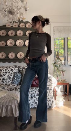 a woman standing in front of a bed wearing high waisted jeans and black shoes