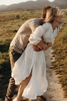 a woman in a white dress is hugging a man on the side of a dirt road