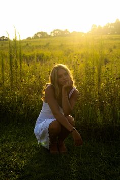 a woman sitting in the grass with her hand on her face and looking at the camera