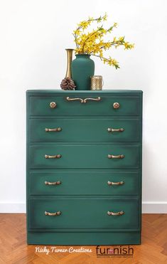 a green dresser with gold handles and flowers in a vase sitting on top of it