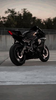 a black motorcycle is parked in an empty parking lot with trees in the back ground