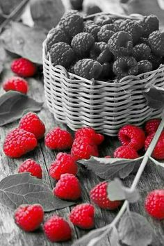 raspberries in a wicker basket on a wooden table with leaves and flowers