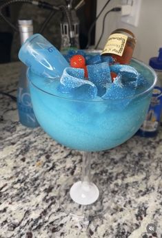 a blue drink in a glass filled with ice and some bottles on top of a counter