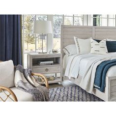 a white bed sitting next to a window with blue curtains and pillows on top of it