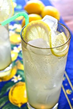 two glasses filled with lemonade and ice sitting on a blue table cloth next to lemons