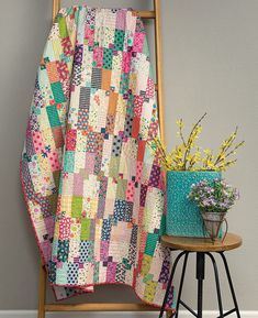 a chair with a quilt on it next to a potted plant