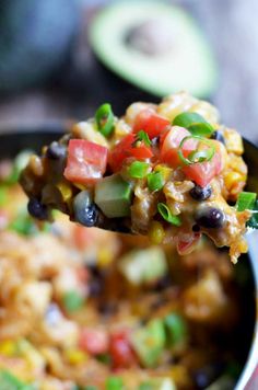 a spoon full of mexican rice and beans with avocado in the background,