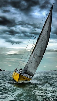 a yellow sailboat in the middle of the ocean under a cloudy sky with dark clouds