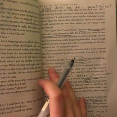 a person is holding a pen and looking at an open book with writing on it