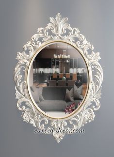 an ornate white frame with a mirror reflecting a living room in the center and furniture on the other side