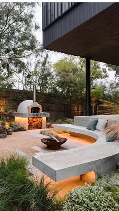 an outdoor living area with concrete furniture and fire pit in the center, surrounded by greenery