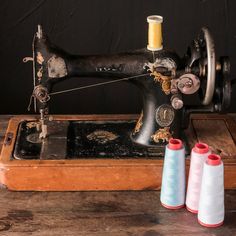 three spools of thread sit next to an old sewing machine on a wooden table