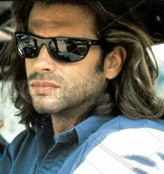 a man with long hair and sunglasses sitting in a car looking off to the side