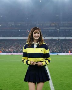 a young woman standing on top of a soccer field wearing a yellow and black striped shirt